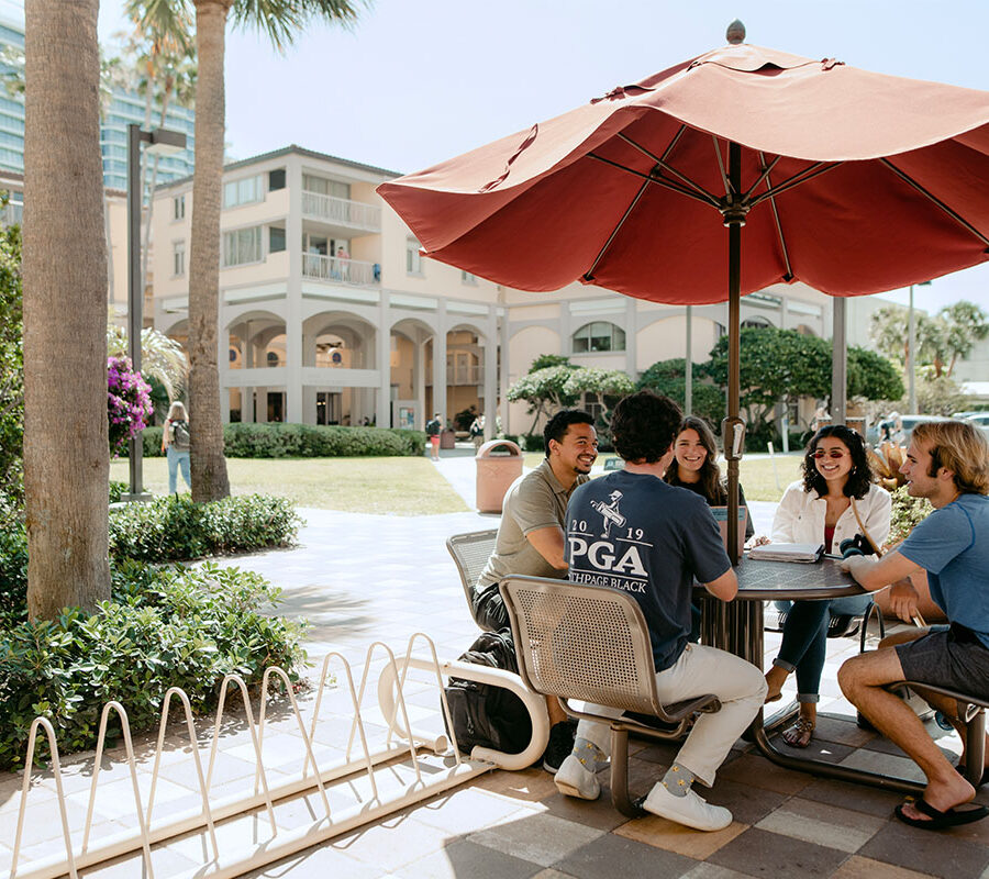Intercultural studies students sit under an umbrella on campus.